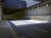 an empty parking lot with light on, and concrete and glass buildings around it and pavement