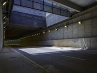 an empty parking lot with light on, and concrete and glass buildings around it and pavement