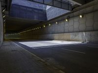 an empty parking lot with light on, and concrete and glass buildings around it and pavement