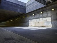 the asphalt road underpass of an empty concrete wall near many lights and buildings, some lighting turned on