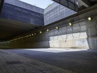 the asphalt road underpass of an empty concrete wall near many lights and buildings, some lighting turned on