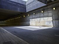 the asphalt road underpass of an empty concrete wall near many lights and buildings, some lighting turned on