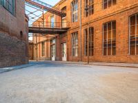 a lone empty street in an old brick building complex with a metal walkway between the buildings