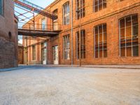 a lone empty street in an old brick building complex with a metal walkway between the buildings