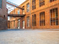 a lone empty street in an old brick building complex with a metal walkway between the buildings