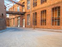 a lone empty street in an old brick building complex with a metal walkway between the buildings