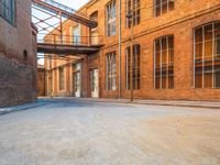 a lone empty street in an old brick building complex with a metal walkway between the buildings