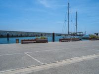 three park benches that are next to each other near water, and a sailboat on the water in the distance