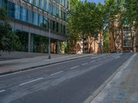 a street next to some buildings and trees along a sidewalk that has two rows of glass windows