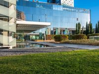 a large glass building with many windows on each of it's sides is surrounded by green grass and trees