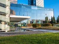 a large glass building with many windows on each of it's sides is surrounded by green grass and trees