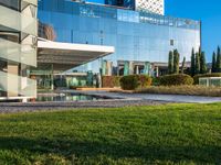 a large glass building with many windows on each of it's sides is surrounded by green grass and trees