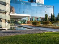 a large glass building with many windows on each of it's sides is surrounded by green grass and trees