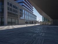 a very large modern looking building with many windows and a person standing outside on the sidewalk