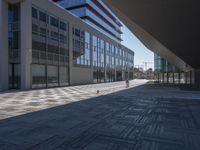 a very large modern looking building with many windows and a person standing outside on the sidewalk