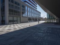 a very large modern looking building with many windows and a person standing outside on the sidewalk