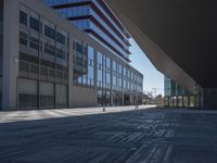 a very large modern looking building with many windows and a person standing outside on the sidewalk