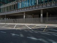 an empty street with tall buildings in the background, some cars in front of a fence and another car parked next to the road