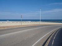 an empty road next to the ocean on a sunny day with blue skies and clouds