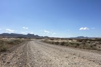 an empty road in a wide open plain of land near mountains and water on a sunny day