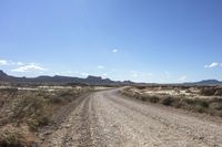 an empty road in a wide open plain of land near mountains and water on a sunny day