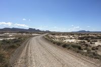 an empty road in a wide open plain of land near mountains and water on a sunny day