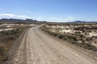 an empty road in a wide open plain of land near mountains and water on a sunny day