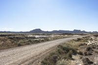 an empty road in a wide open plain of land near mountains and water on a sunny day