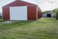 a barn and another building on the other side of a green field with a dirt path in front