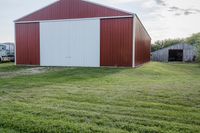 a barn and another building on the other side of a green field with a dirt path in front
