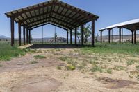 a barn with an open roof is located in a field of dry grass and a grassy area behind it