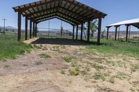 a barn with an open roof is located in a field of dry grass and a grassy area behind it