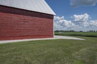 a barn on top of a gravel road next to grass and trees in front of a blue sky