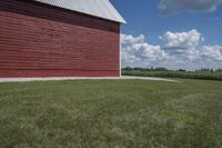 a barn on top of a gravel road next to grass and trees in front of a blue sky