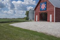 a barn on top of a gravel road next to grass and trees in front of a blue sky