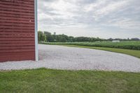 a barn and gravel path on the farm with trees in the background on a cloudy day