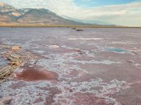 a vast, barren desert area with various colorful structures and water features, with mountains in the distance