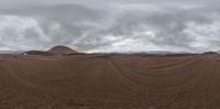 a long view of a barren desert area with lots of clouds and sand on the ground