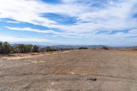 a wide view of a barren field with a dirt road in the foreground, and mountains to the side