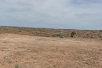 the view of a barren field and dry grass on a clear day with grey clouds