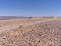 a barren highway running on top of a hill covered in brown rock and grass near water