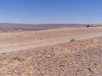 a barren highway running on top of a hill covered in brown rock and grass near water