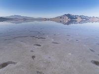 this photo was taken from an airplane window of a barren land, with small clouds and mountains reflecting in the water