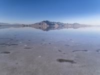 this photo was taken from an airplane window of a barren land, with small clouds and mountains reflecting in the water