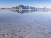 this photo was taken from an airplane window of a barren land, with small clouds and mountains reflecting in the water