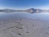 this photo was taken from an airplane window of a barren land, with small clouds and mountains reflecting in the water