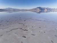 this photo was taken from an airplane window of a barren land, with small clouds and mountains reflecting in the water