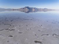 this photo was taken from an airplane window of a barren land, with small clouds and mountains reflecting in the water