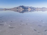 this photo was taken from an airplane window of a barren land, with small clouds and mountains reflecting in the water