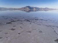 this photo was taken from an airplane window of a barren land, with small clouds and mountains reflecting in the water